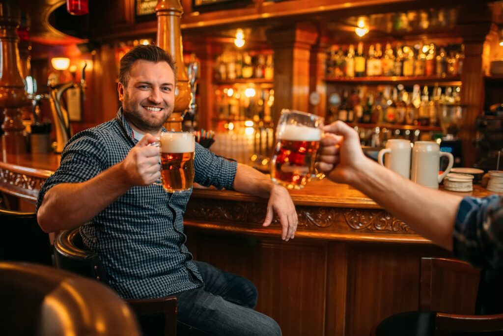 Two male friends drinks beer at the counter in pub